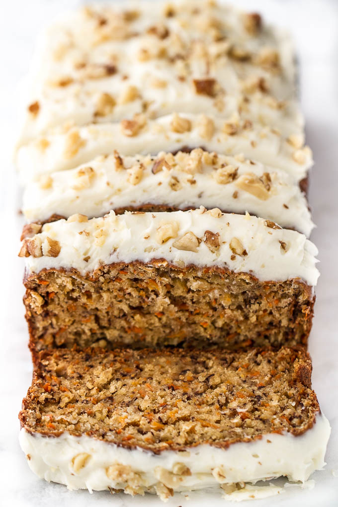 Sliced carrot cake banana bread with cream cheese frosting and chopped walnuts on top.