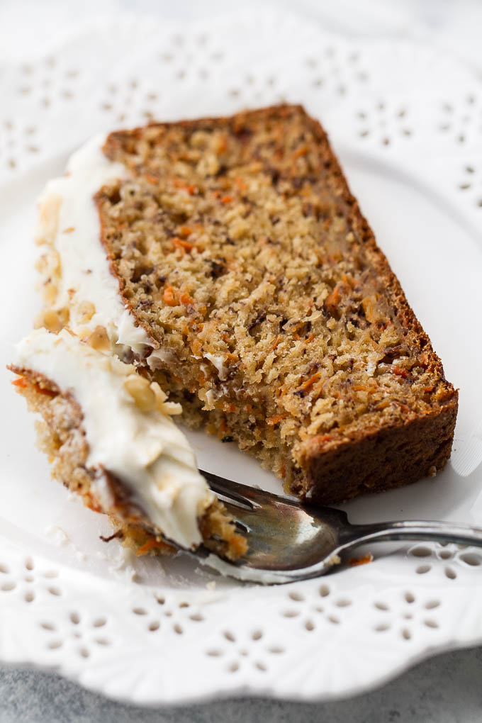 A slice of carrot cake banana bread on a plate with a fork taking out a bit of it.