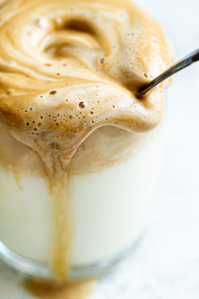 A closeup of a cup of dalgona coffee with foam dripping down the side.