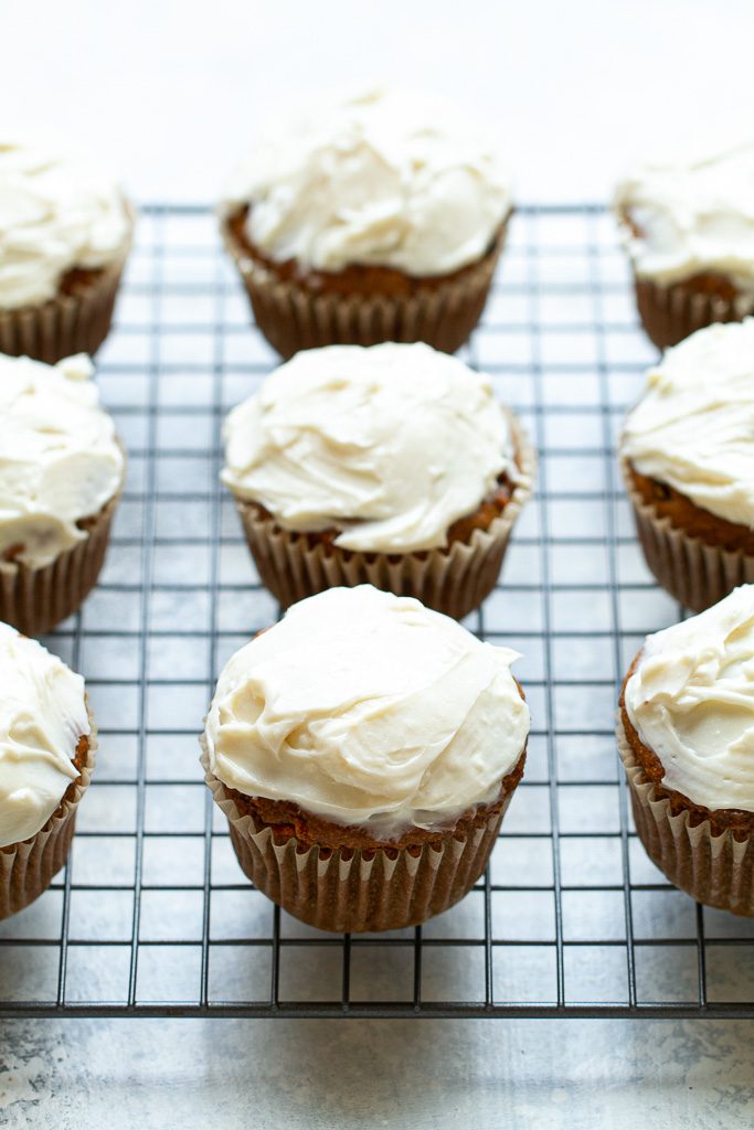 Flourless carrot cake muffins with cream cheese frosting on a cooling tray.