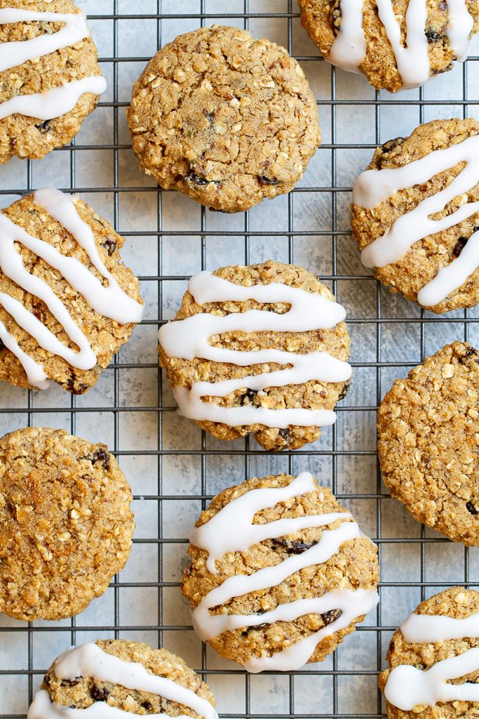 A top view of flourless oatmeal raisin cookies sitting on a cooling rack with some cookies iced and others plain.