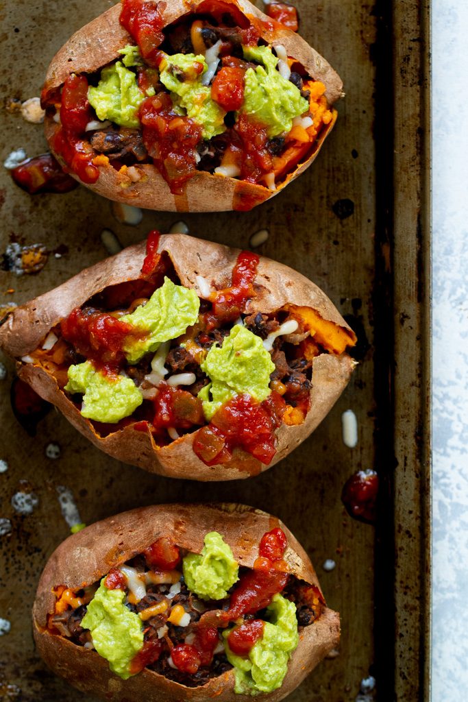 Taco stuffed sweet potatoes topped with avocado and salsa.