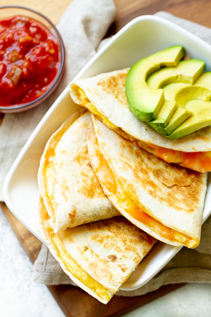 Breakfast quesadillas on a plate with some avocado and salsa.
