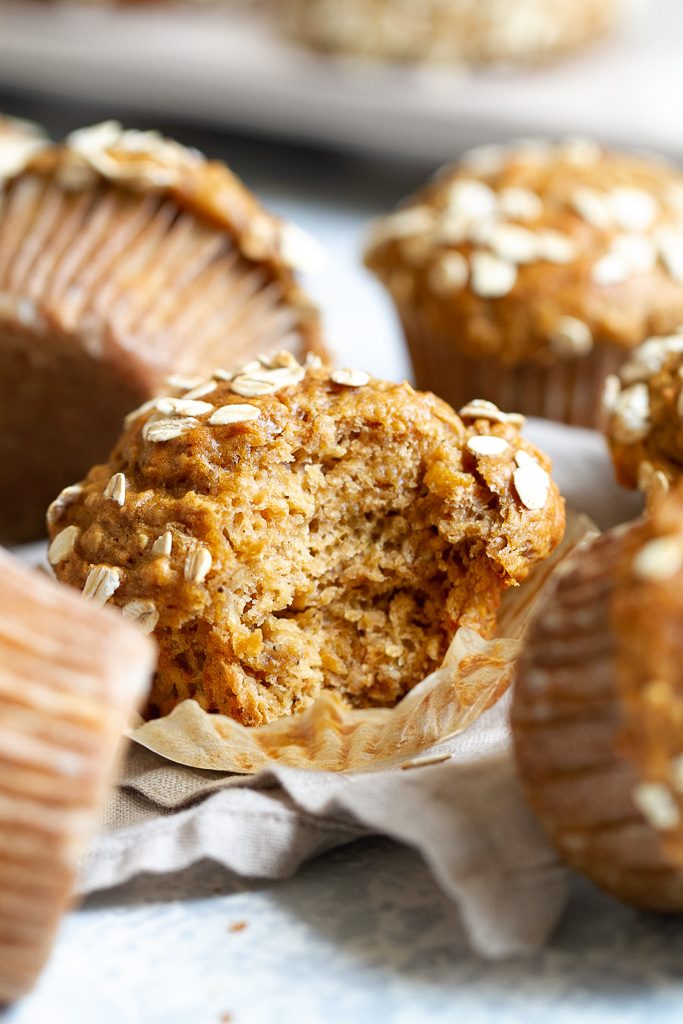 A healthy banana oat muffin with a bite taken out of it so that you can see the fluffy texture inside of it.